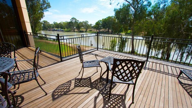 A wooden deck with outdoor furniture, a view of a river, and a metal railing.