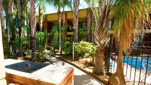 A poolside area with a brick bench, palm trees, and a building with balconies in the background.