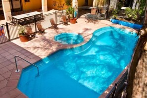Une piscine au design incurvé, entourée d’une terrasse carrelée et de mobilier d’extérieur.