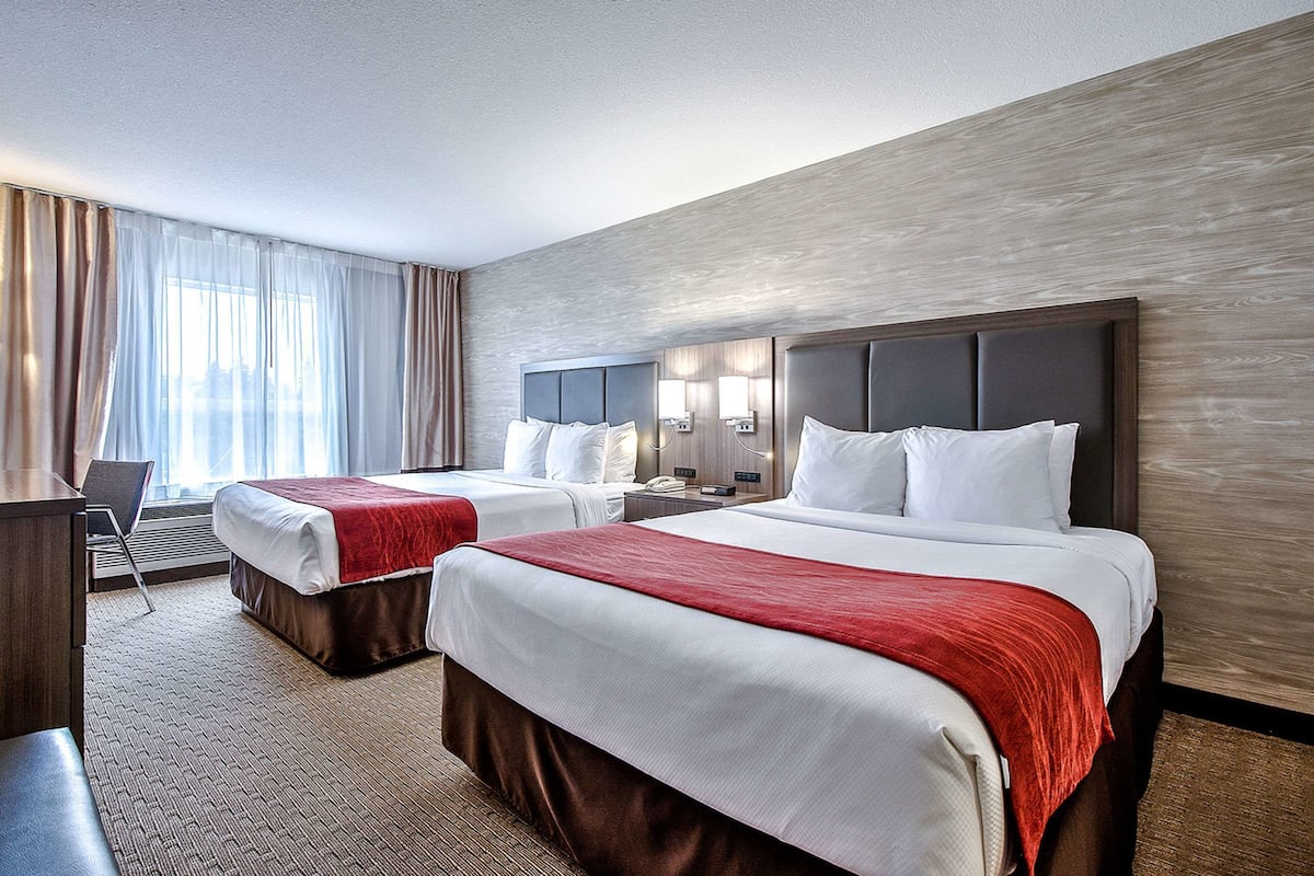 A hotel room with two beds, a desk, and a chair.