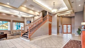 A spacious lobby with a wooden staircase, a fireplace, and a large window with a view. - Comfort Inn And Suites South (Calgary)