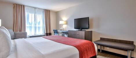 Una habitación de hotel con una cama grande, un escritorio, un televisor y un banco.
