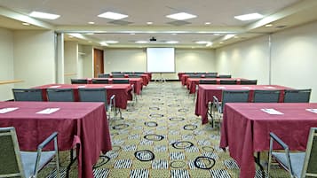 A conference room with multiple tables and chairs, a projector screen, and a carpeted floor.