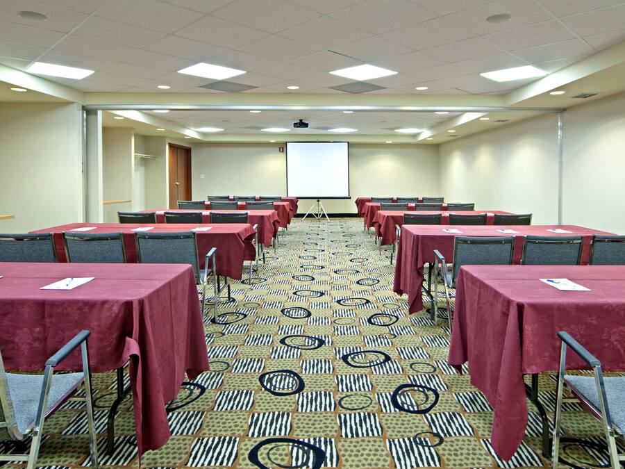 A conference room with multiple tables and chairs, a projector screen, and a carpeted floor.