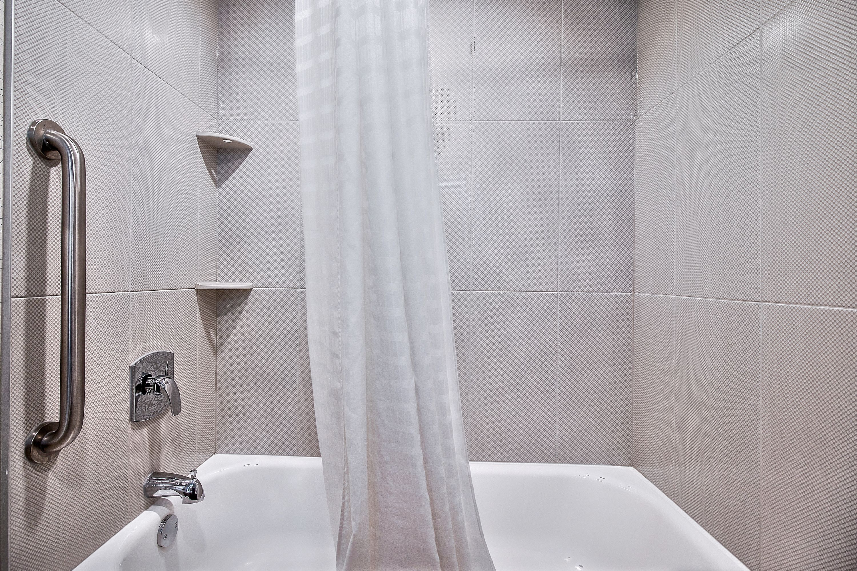 Un baño moderno con una bañera blanca, una cortina de ducha y un asidero.