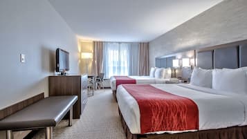 A hotel room with two beds, a desk, a bench, and a television.