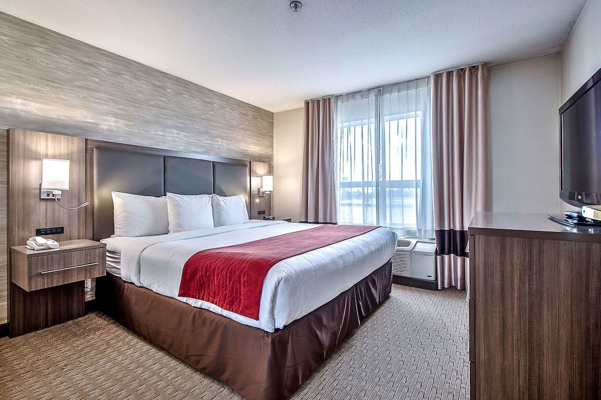 A hotel room with a large bed, a desk with a telephone, a flat-screen TV, and a window with curtains.