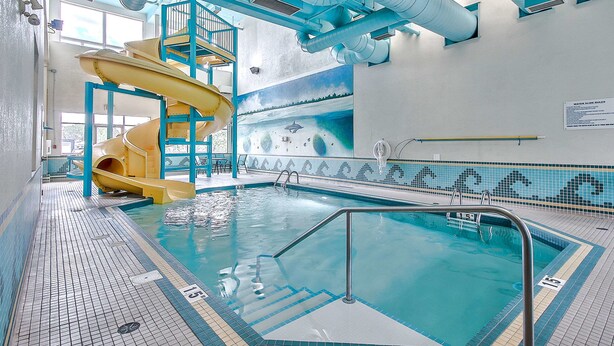 An indoor swimming pool with a yellow slide, clear water, and tiled flooring. - Comfort Inn And Suites South (Calgary)