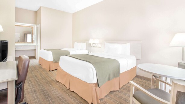 A hotel room with two beds, a desk, a chair, a small table, and a mirror. - Baymont by Wyndham Crestview (Crestview)