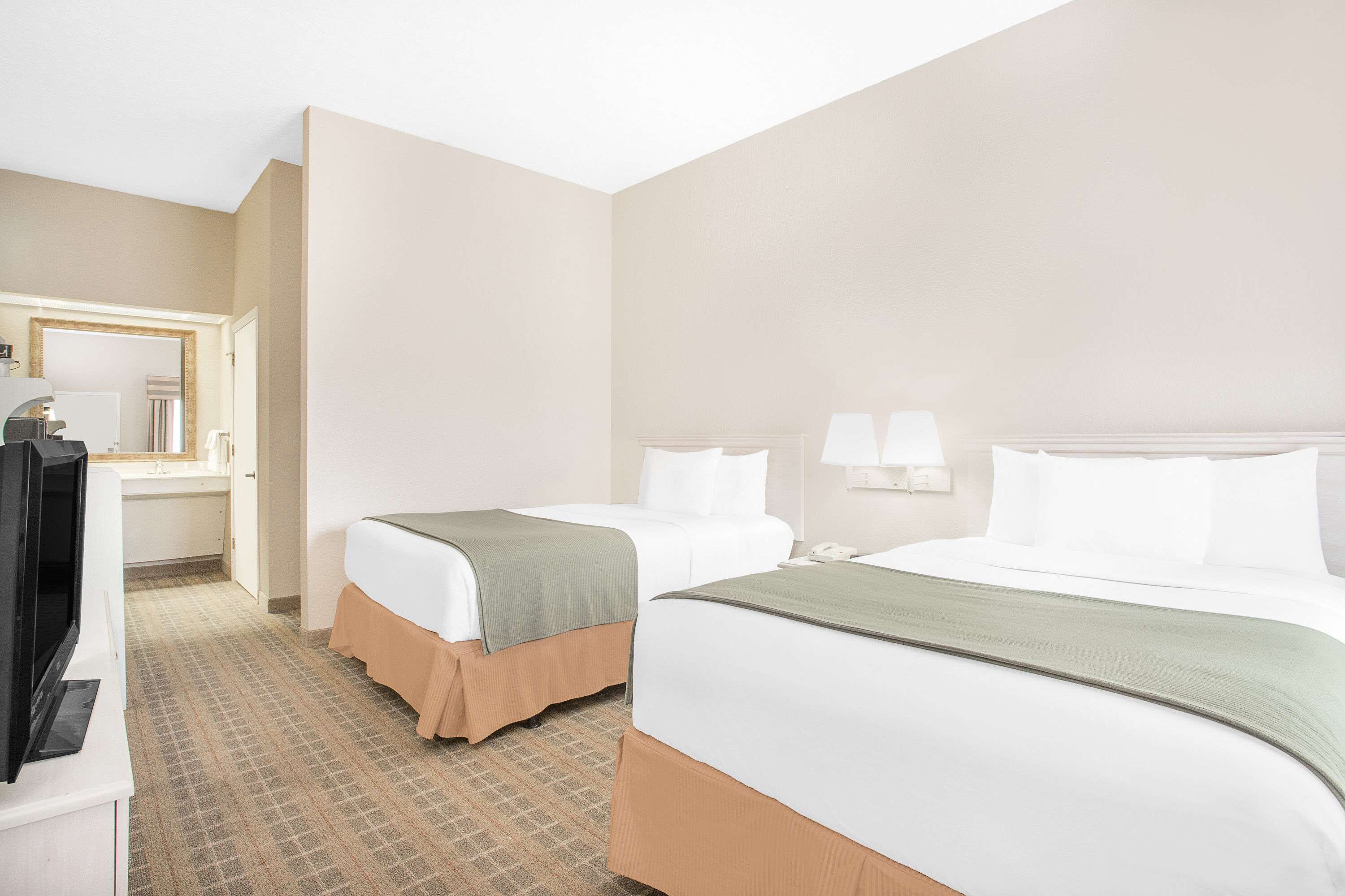 Habitación de hotel con dos camas, un televisor y un baño visible a través de una puerta abierta.