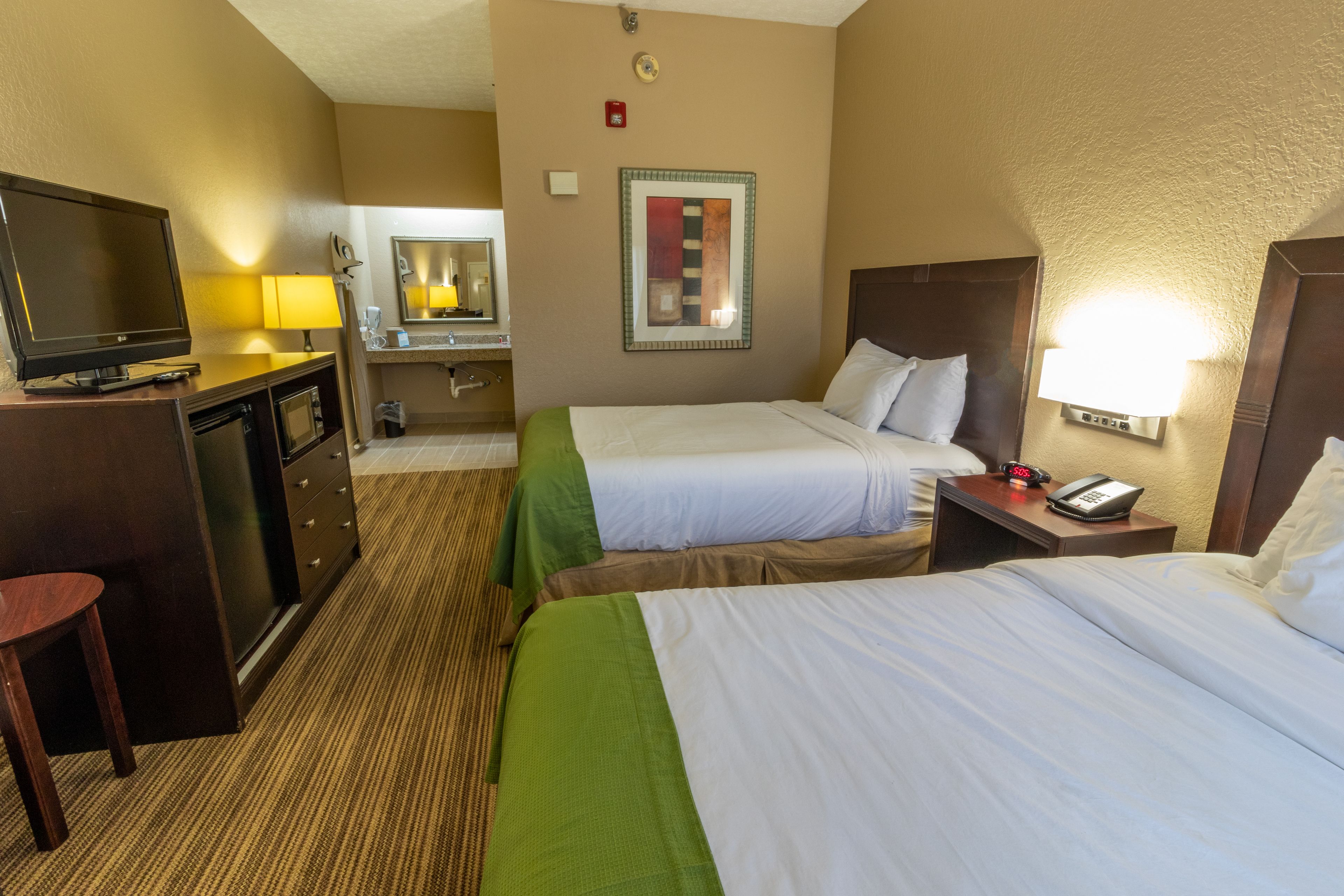 Una habitación de hotel con dos camas, un escritorio con televisor, un espejo y una lámpara.