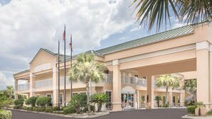 A multi-story hotel with a covered entrance, palm trees, and American flags. - Baymont by Wyndham Crestview (Crestview)