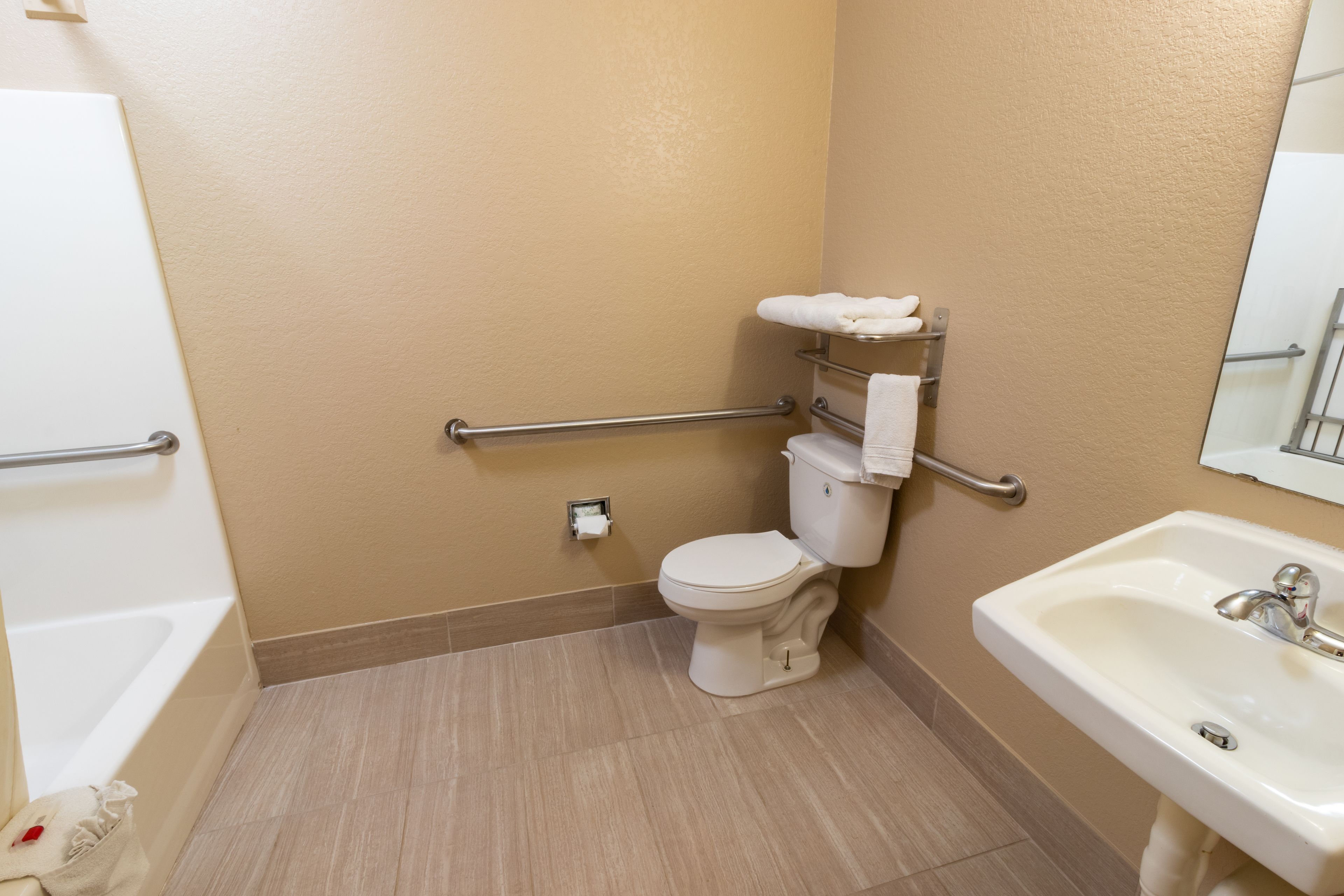 A bathroom with a white toilet, a sink, and a bathtub. There are grab bars installed near the toilet and sink.