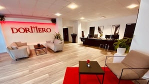 A modern hotel lobby with a red carpet, sofas, a coffee table, and a reception desk. - DORMERO Hotel Bretten (Bretten)