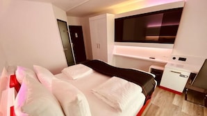 A modern hotel room with a large bed, a TV mounted on the wall, and a small desk with a chair. - DORMERO Hotel Bretten (Bretten)