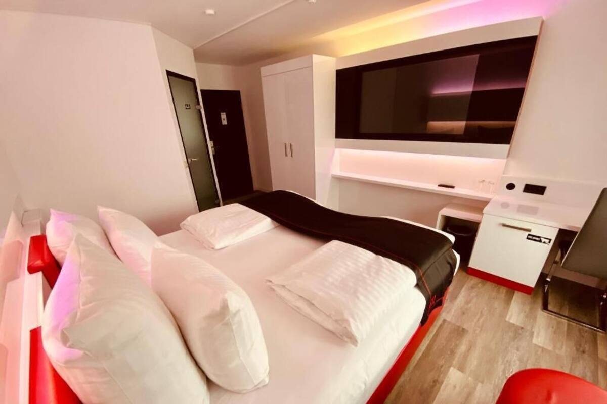 A modern hotel room with a large bed, a TV mounted on the wall, and a small desk with a chair.