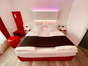 A modern hotel room with a large bed, red accents, and a minimalist design. - DORMERO Hotel Bretten (Bretten)