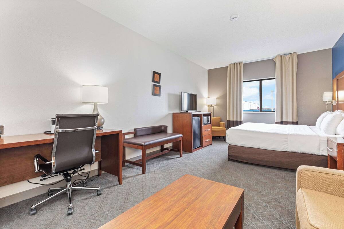 A hotel room with a desk, chair, bed, and a TV.