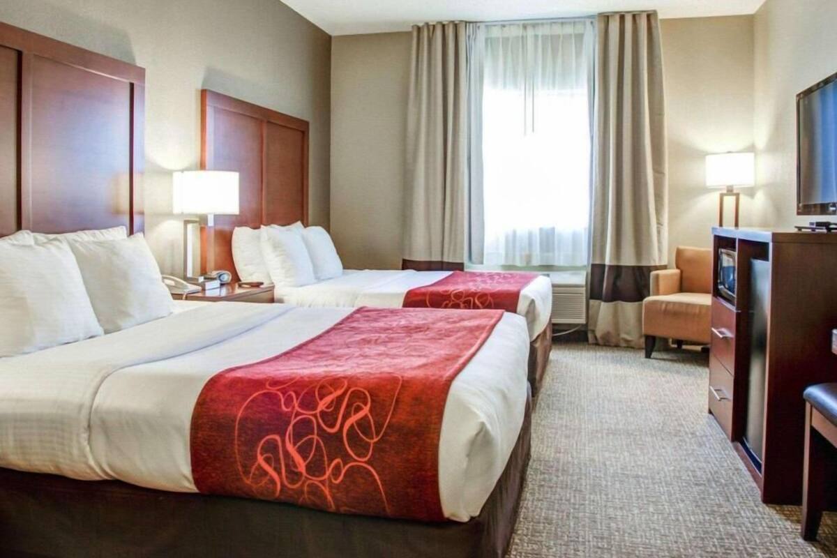 A hotel room with two beds, a desk, a chair, a TV, and a window with curtains.