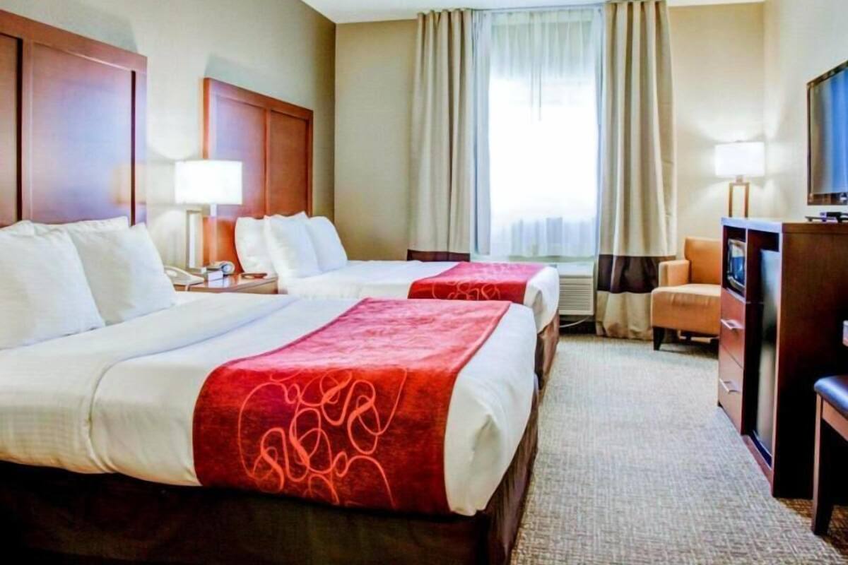 A hotel room with two beds, a desk, a chair, a TV, and a window with curtains.