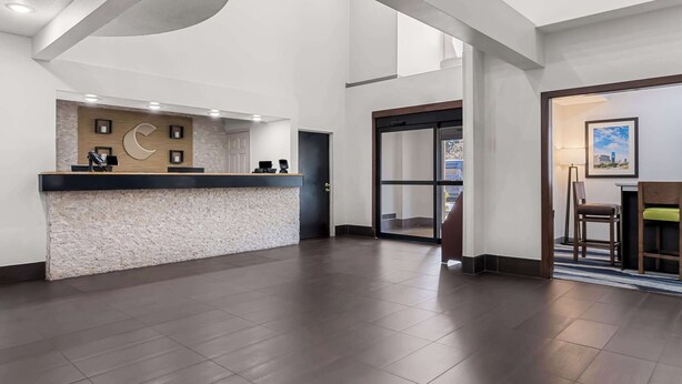 A hotel reception area with a reception desk, a large window, and a door leading to the lobby. - Comfort Inn & Suites near Tinley Park Amphitheater (Tinley Park)