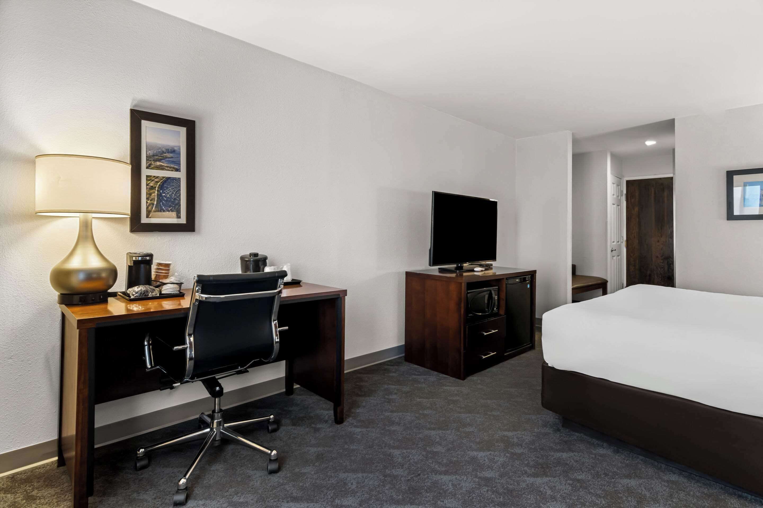A hotel room with a bed, desk, chair, TV, lamp, and a framed picture on the wall.