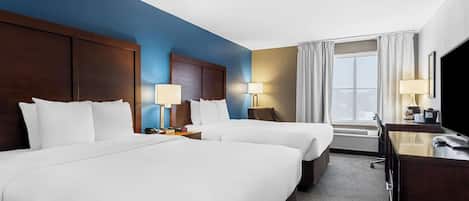 A hotel room with two beds, a desk, and a large window with curtains.