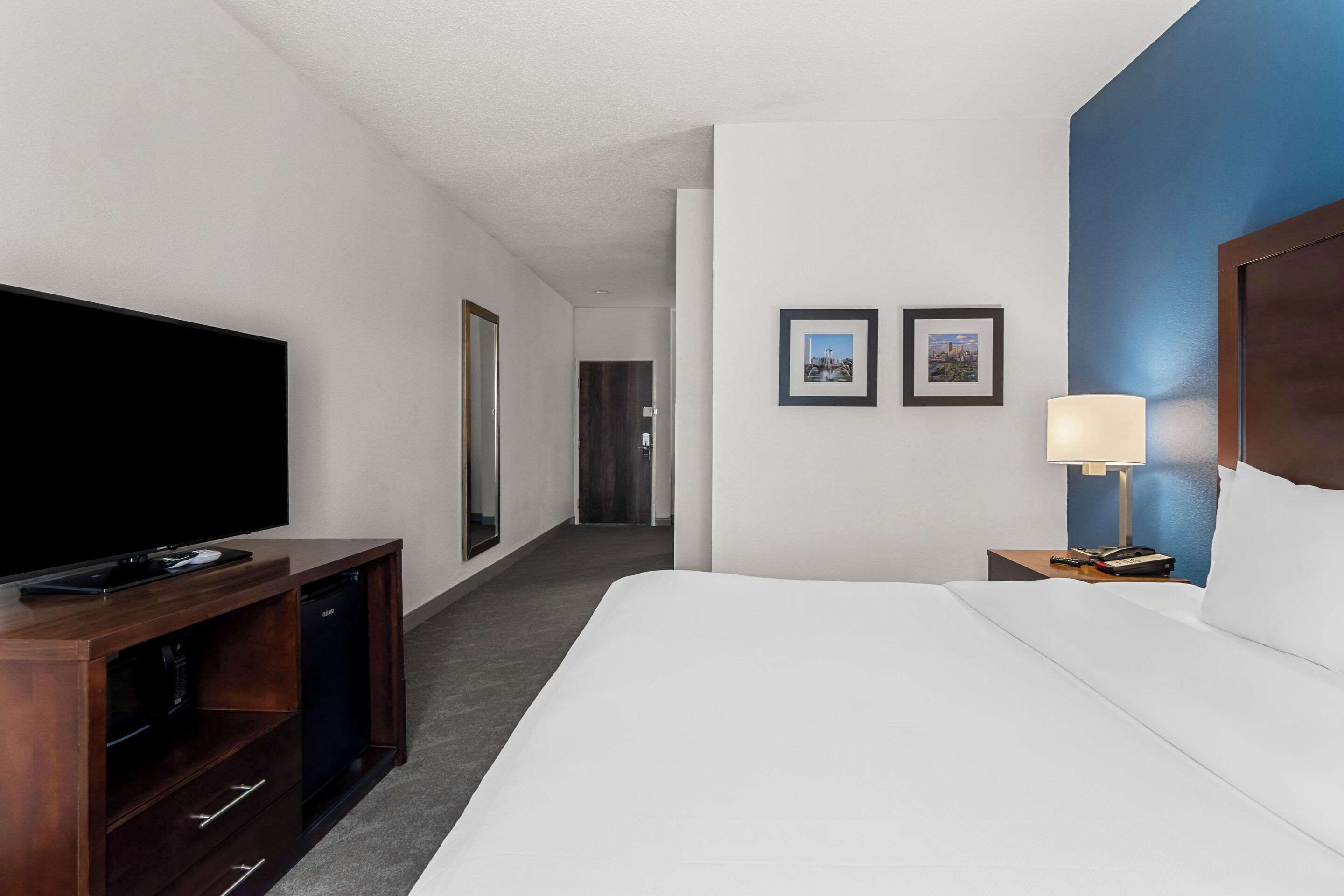 Een hotelkamer met een groot bed, een flatscreen televisie, een houten dressoir en twee ingelijste foto's aan de muur.