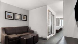 A hotel room with a brown sofa, a small coffee table, and a bed with white linens. There are three framed pictures on the wall. - Comfort Inn & Suites near Tinley Park Amphitheater (Tinley Park)