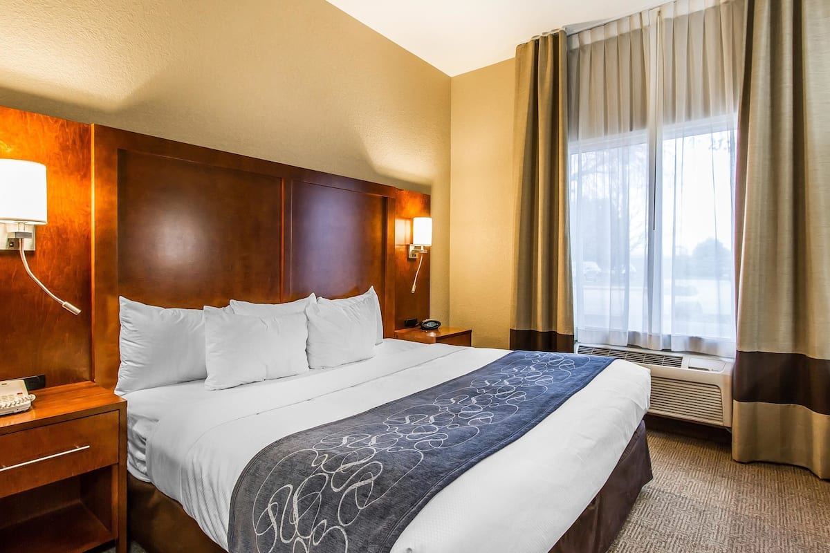 A hotel room with a large bed, wooden headboard, bedside lamps, a telephone, and a window with curtains.