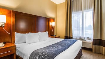 Habitación de hotel con una cama grande, cabecera de madera, lámparas de noche, un teléfono y una ventana con cortinas.