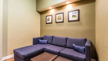 Un sofá modular con un reposapiés marrón, un cuadro con tres imágenes colgado en la pared, e iluminación empotrada en el techo.