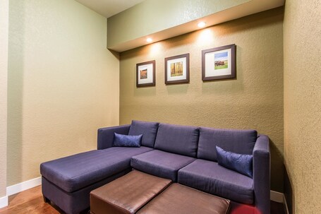 A sectional sofa with a brown ottoman, a wall-mounted picture frame with three pictures, and recessed ceiling lighting.