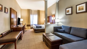 Ett hotellrum med en säng, en soffa, ett skrivbord med en dator, en tv och ett fönster med gardiner.