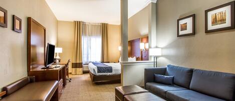 Quarto de hotel com cama, sofá, escrivaninha com computador, televisão e janela com cortinas.
