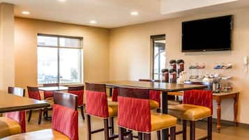 Un comedor de hotel con varias mesas y sillas, un televisor de pantalla plana en la pared y una estación de café con diferentes opciones.