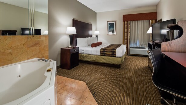 Une chambre d’hôtel avec une grande baignoire, un lit recouvert d’une courtepointe à motifs, un bureau avec un ordinateur et un téléviseur.
