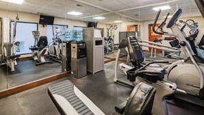 Une salle de sport équipée de divers appareils d’exercice, d’un distributeur d’eau et d’un miroir.