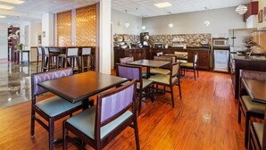 Un restaurant avec des tables et des chaises en bois, un comptoir avec une machine à café et un mur décoratif orné d’un motif.