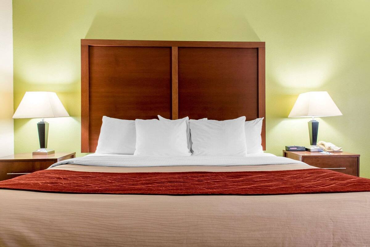 A hotel room with a bed, two bedside tables, lamps, and a wooden headboard.