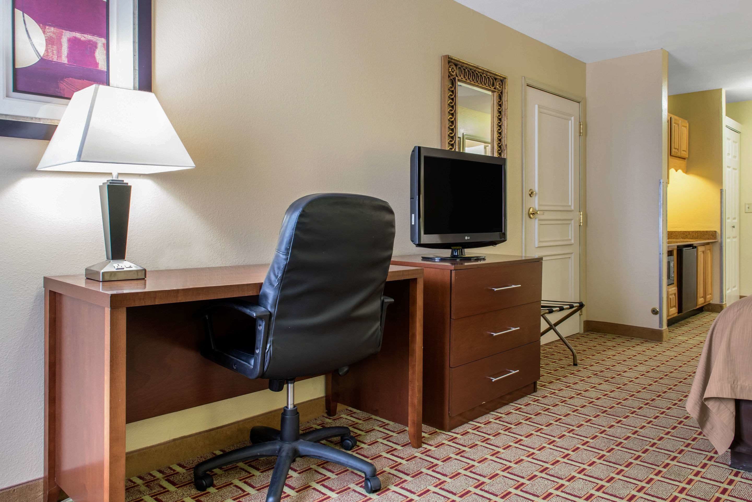 Een hotelkamer met een bureau, een stoel, een televisie, een lamp, een spiegel en een kamer met een patroon.