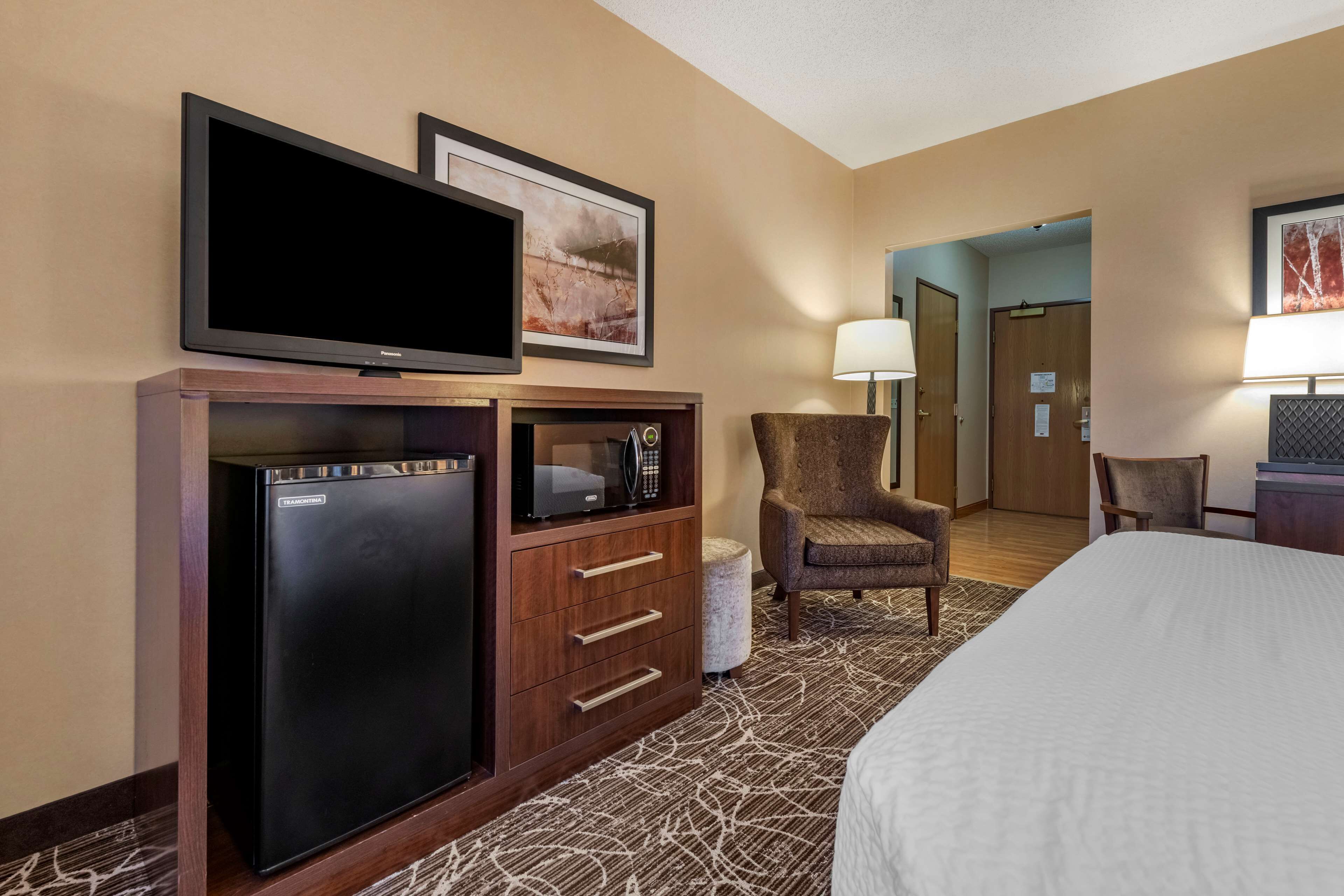 A hotel room with a bed, a desk with a refrigerator, a microwave, a chair, and a television.