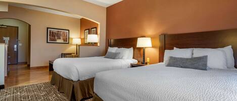 A hotel room with two beds, a wooden headboard, a patterned rug, and a framed picture on the wall.
