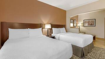 A hotel room with two beds, a nightstand, a lamp, a mirror, and a framed picture on the wall.