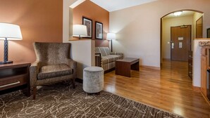A hotel lobby with a wooden floor, a brown armchair, a striped sofa, a small round ottoman, and a wooden coffee table. - Best Western Plus Chelsea Hotel (Monticello)
