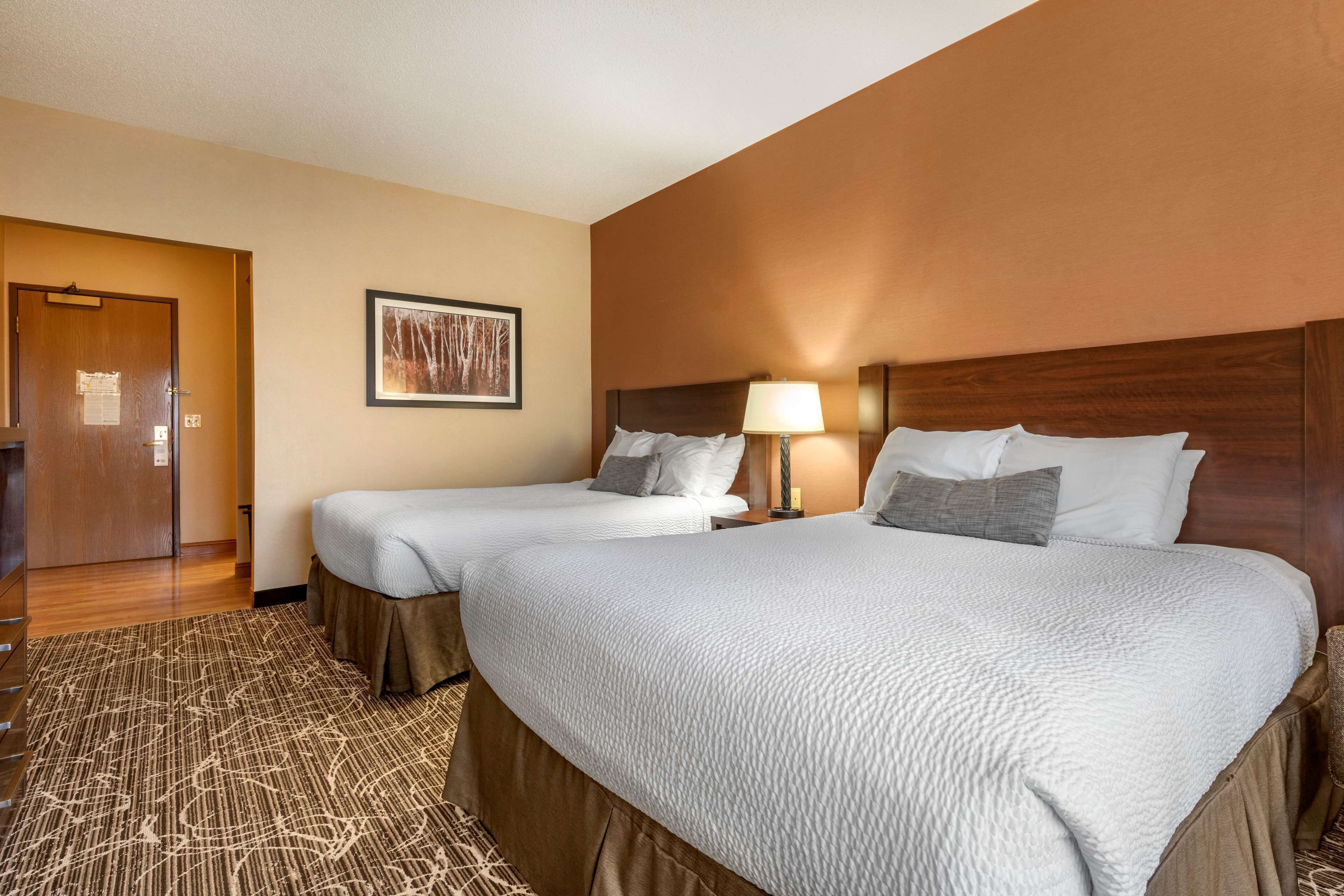 A hotel room with two beds, a wooden headboard, a framed picture on the wall, and a carpeted floor.