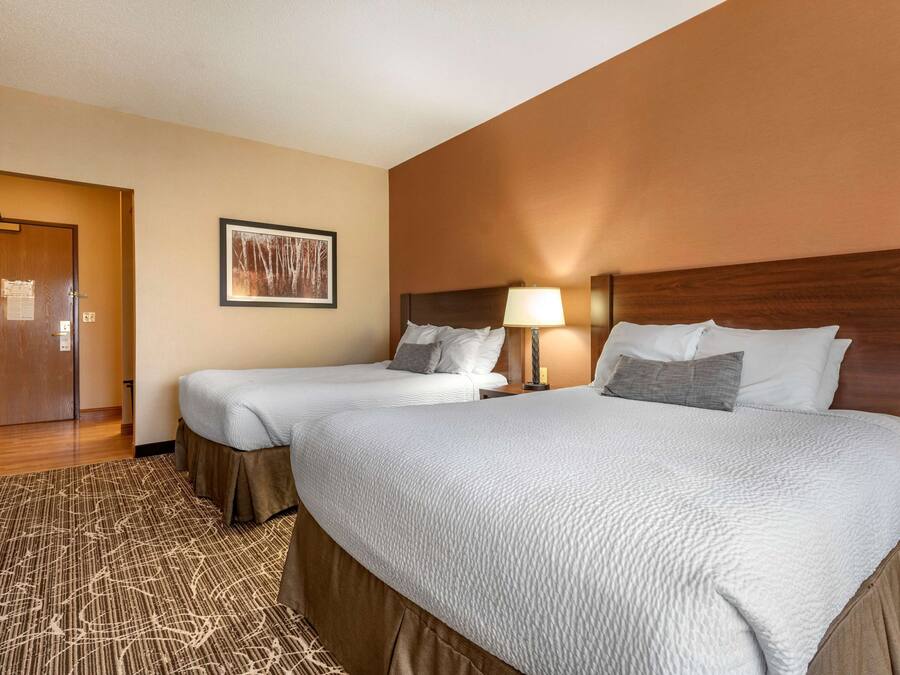 A hotel room with two beds, a wooden headboard, a framed picture on the wall, and a carpeted floor.
