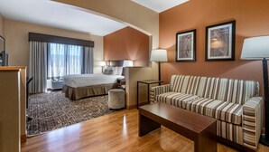 A hotel room with a bed, a sofa, a coffee table, a lamp, and framed artwork on the wall. - Best Western Plus Chelsea Hotel (Monticello)