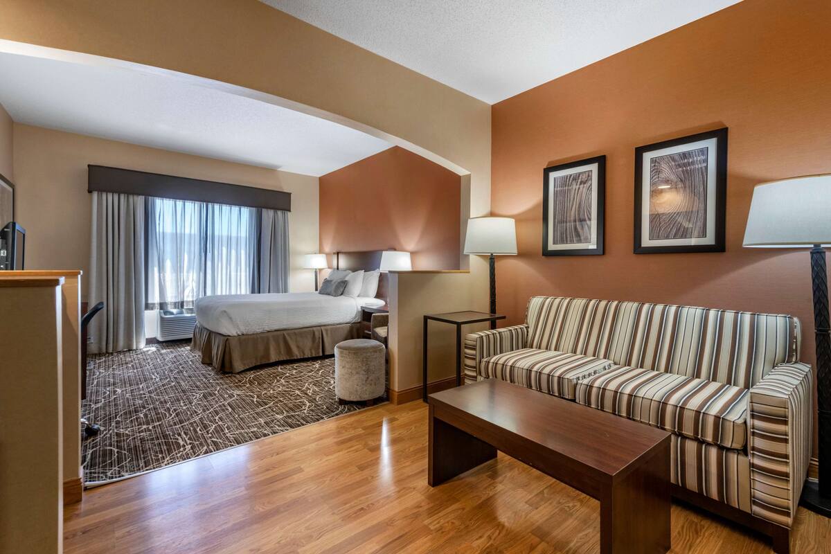 A hotel room with a bed, a sofa, a coffee table, a lamp, and framed artwork on the wall.