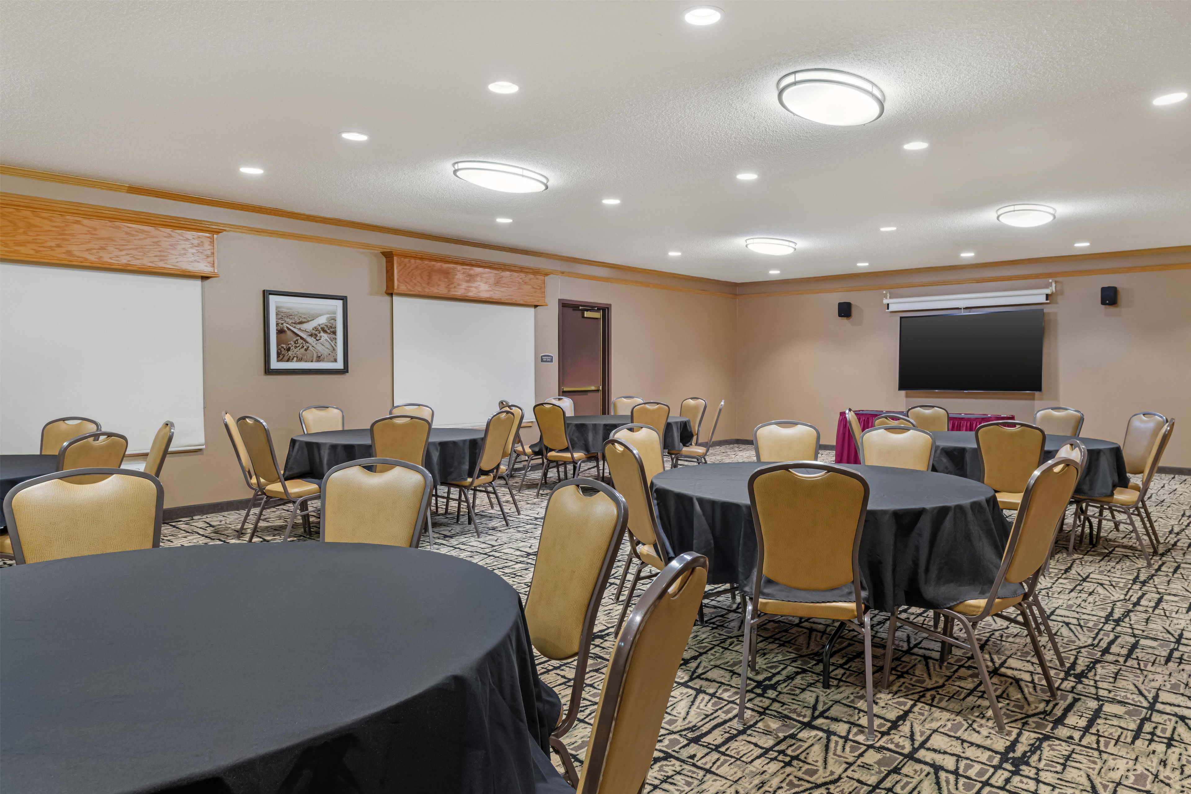 Un salón de conferencias con varias mesas y sillas, una pantalla de proyector y una pizarra.